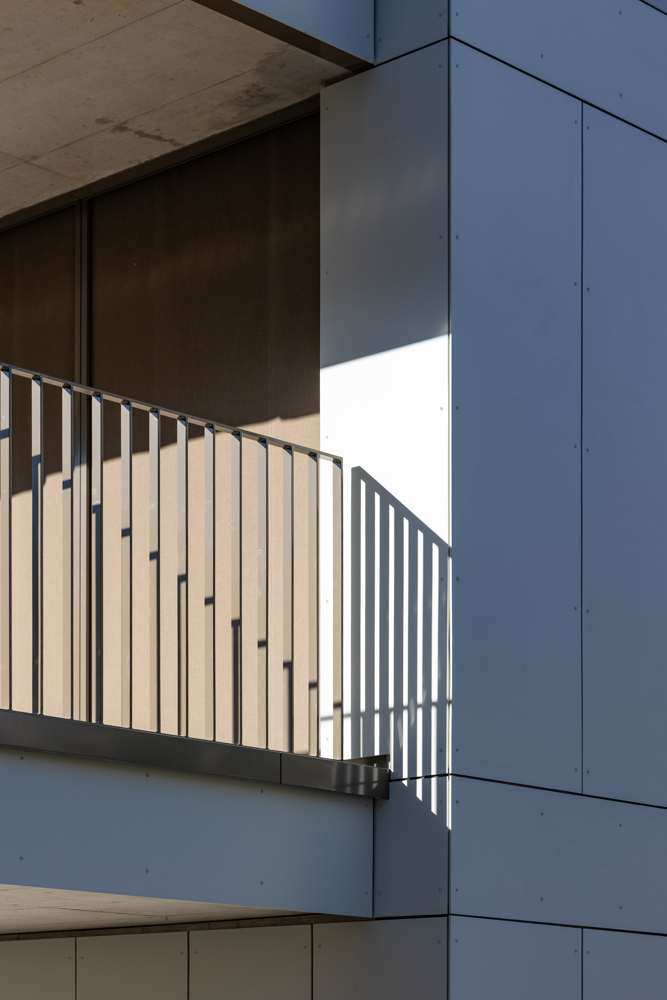 Balkongeländer an der Gebäudeecke: Flachstahlstaketen, verdeckt am Plattenrand befestigt – das Licht zeichnet das Raster auf die Fassade.
