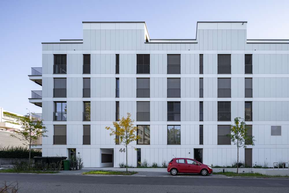 Strassenfassade Haus 44: Lochfassade im Plattenraster, Rafflamellenstoren und französische Balkone; im Erdgeschoss der Hauseingang als Einschnitt.