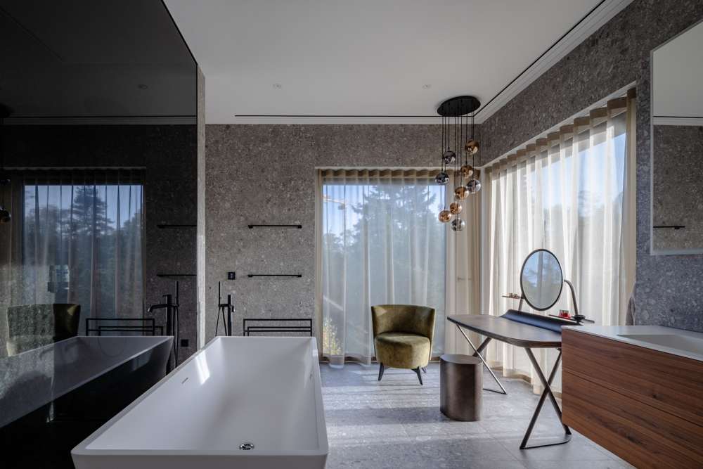 Bad im Penthouse: Feinsteinzeug an Wand und Boden durchlaufend, freistehende Wanne, Vorhänge zur Terrasse.