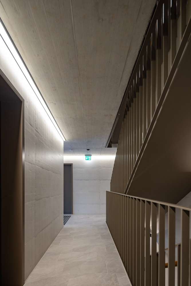 Treppenhaus: Sichtbeton, Lichtlinie unter der Decke, Stabgeländer in dunklem Olivton.