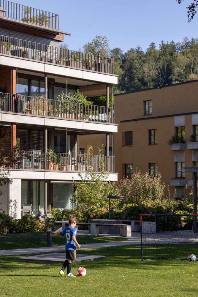 Vom Park: die begrünten Balkonschichten über der Spielwiese, dahinter der Baumbestand.