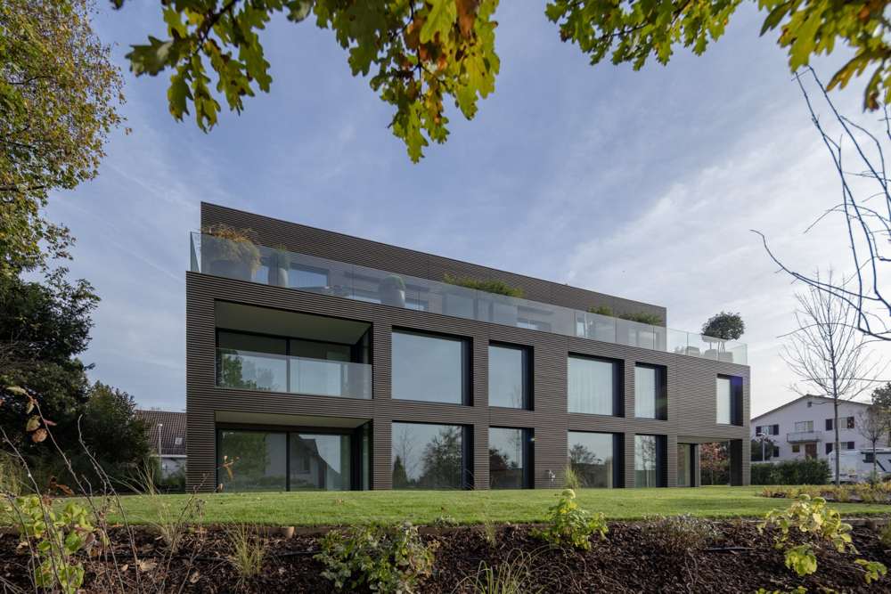 Gartenseite aus der Froschperspektive: die Lochfassade mit geschosshohen Öffnungen, darüber der Dachgarten hinter der Glasbrüstung; Fassade und Dachkante gleich ausgebildet.