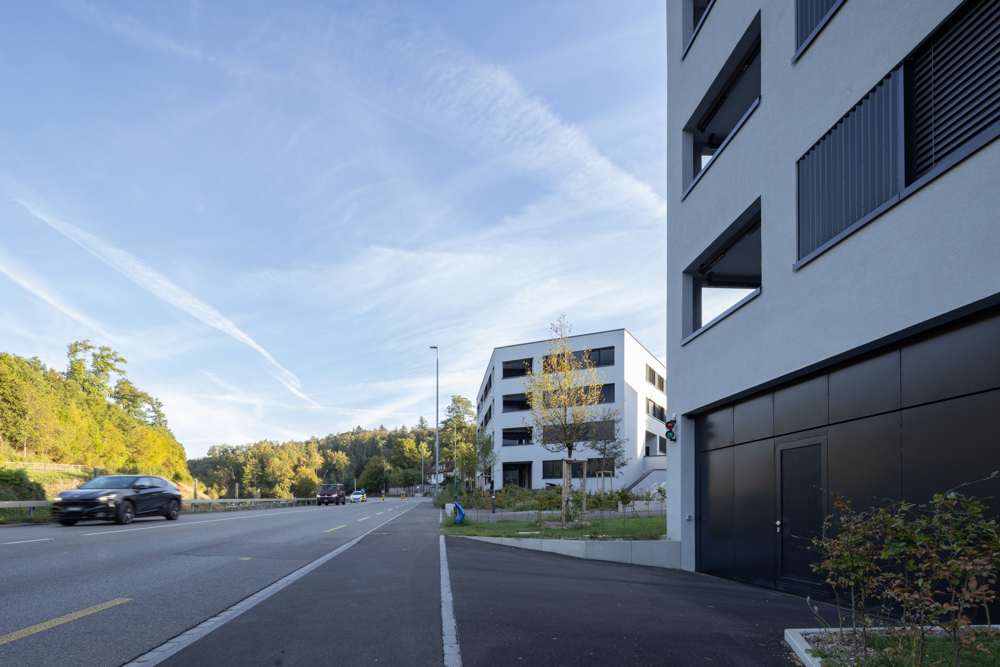 Zufahrt zur Einstellhalle: Das Tor aus dunklen Metallpaneelen sitzt bündig im Sockel des Hauses; dahinter öffnet sich der gemeinsame Freiraum.