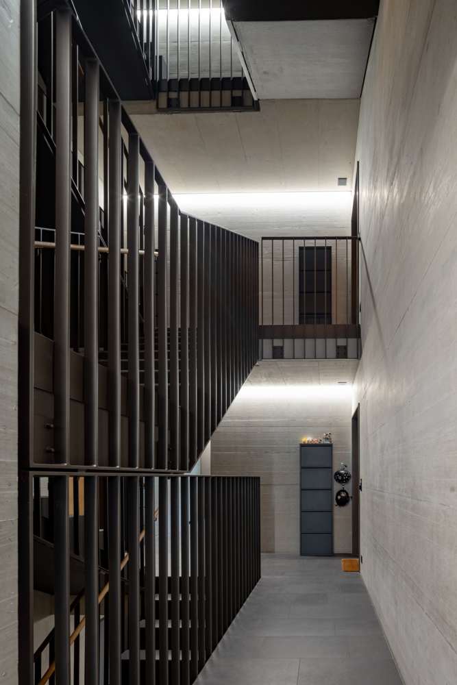 Treppenhaus: Stahlgeländer als durchlaufendes Stabgitter, Sichtbeton, Lichtlinie unter der Decke.