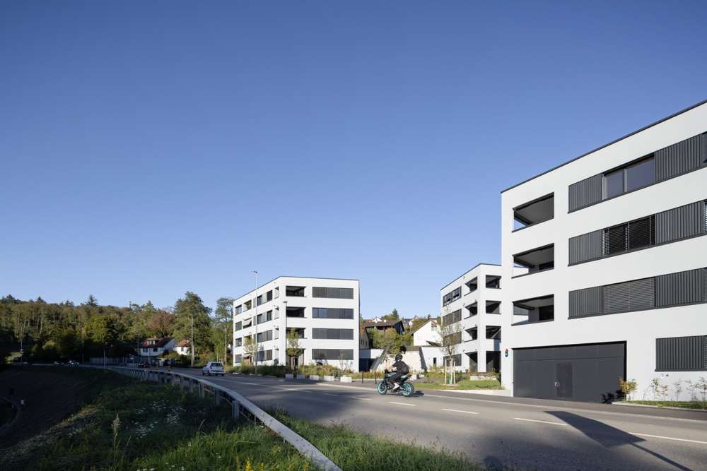 Strassenansicht: Die weissen Baukörper fassen den Strassenraum, eingeschnittene Loggien und dunkle Brüstungsbänder gliedern die Fassaden, die Einfahrt zur Einstellhalle liegt im Sockel des vorderen Hauses.