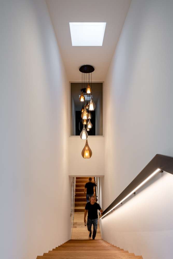Penthouse: Holztreppe mit beleuchtetem Handlauf unter dem Oberlicht, Pendelleuchten im Luftraum.