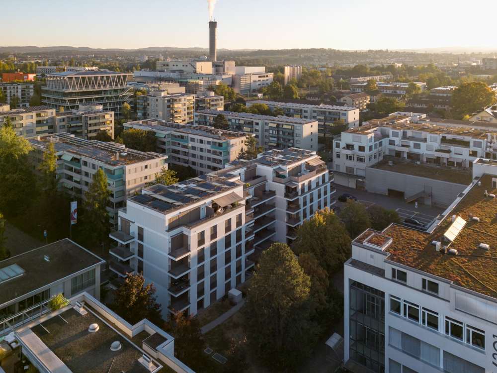 Aus der Luft: die Baukörper Ost und West auf dem Sockel der Einstellhalle, Photovoltaik auf den Dächern; dahinter Oerlikon mit dem Kamin der Kehrichtverwertung.