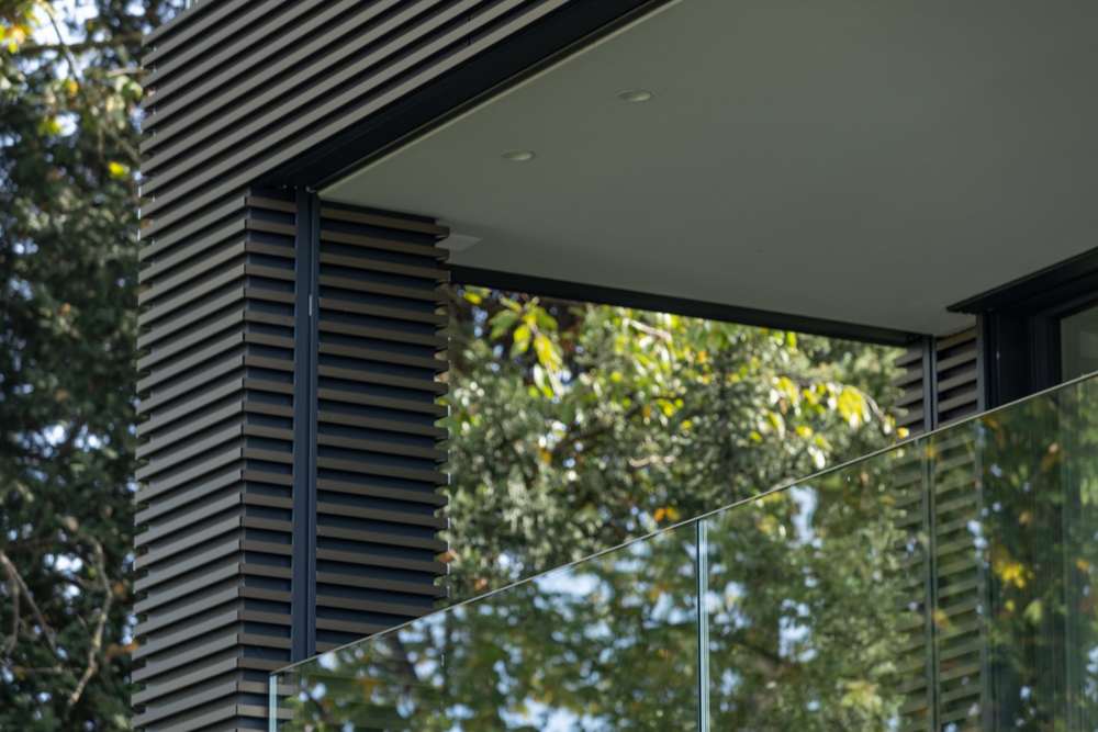 Loggia im Obergeschoss: Die Aluminiumprofile laufen um die Ecke in die Leibung, Rafflamellen und Glasbrüstung, die Untersicht als glatte Fläche.