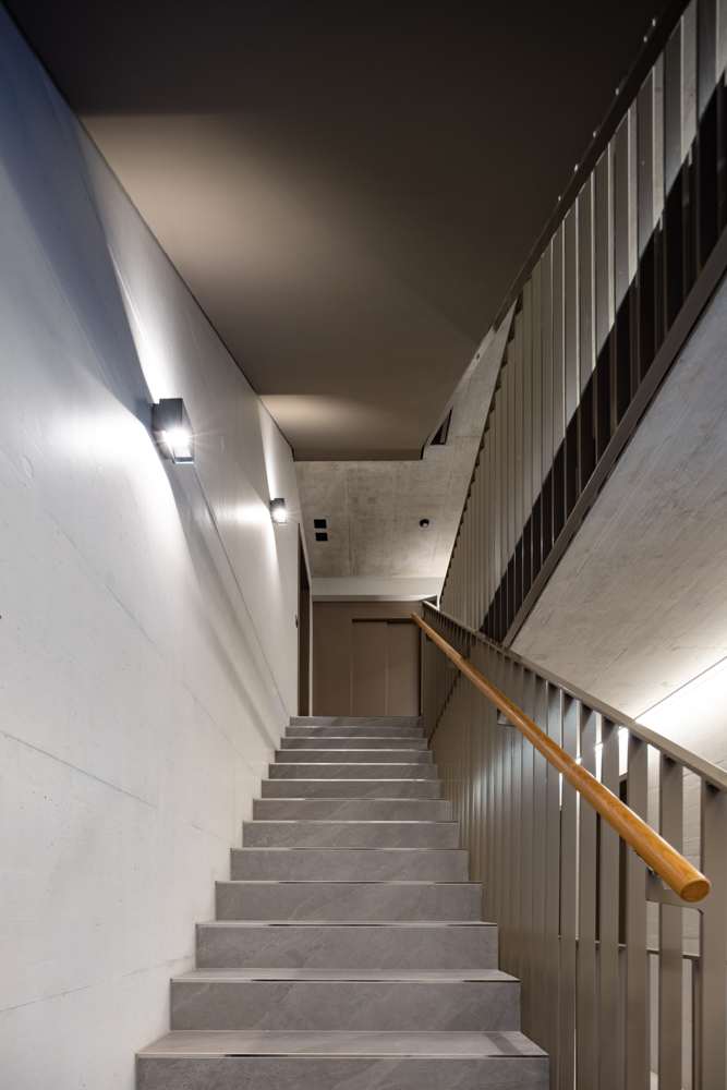 Treppenhaus in Sichtbeton: Stufen in Feinsteinzeug, Wandleuchten, Geländer aus Flachstahl mit Handlauf in Eiche.