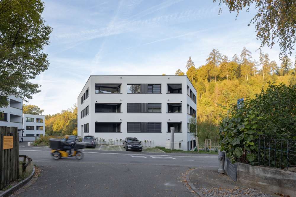 Das Haus am Waldrand: Die kubische Form wird durch die eingeschnittenen Loggien und die Fensterbänder in Raster und Tiefe gegliedert, dahinter steigt der Hang an.